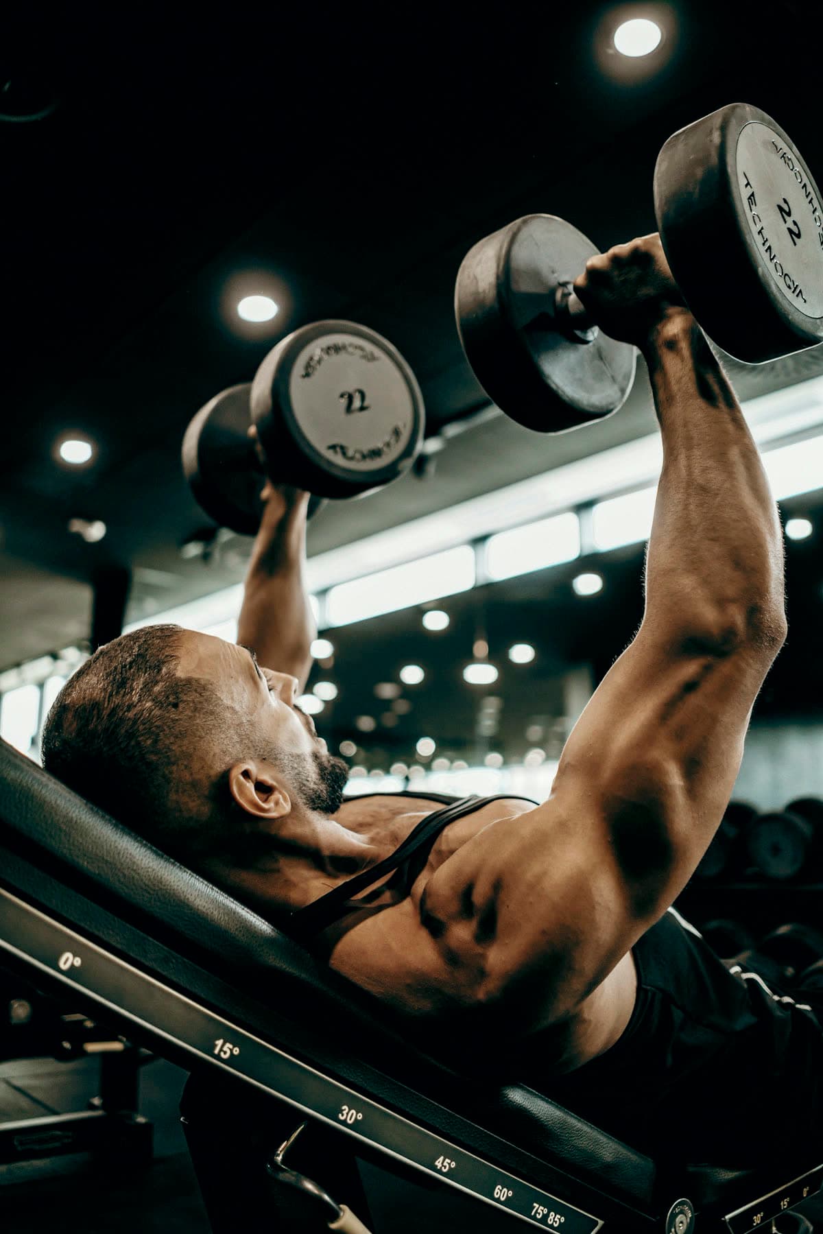 A member pressing two dumbbells on an incline bench